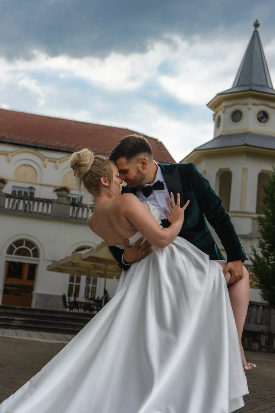 Mladoženja ljubi mladu ispred zgrade sa tornjem