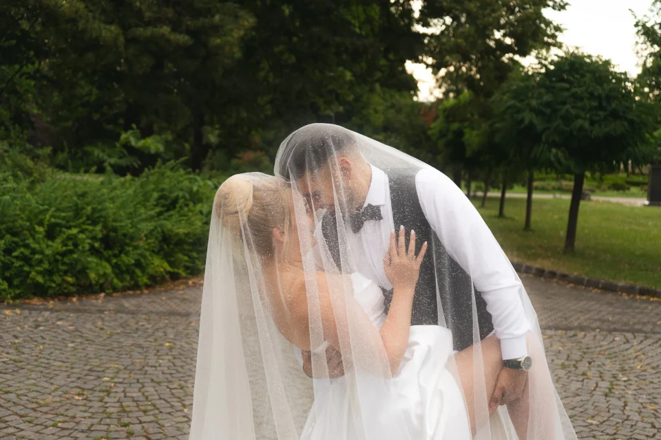 Mladenci se ljube ispod vela na stazi u parku